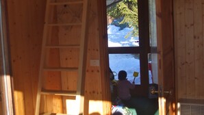 Interior de madera con una escalera que lleva a una ventana, un niño jugando afuera y un bolso en el suelo.