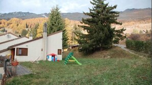 Una propiedad residencial con una casa blanca, un tobogán verde y un gran árbol de coníferas.
