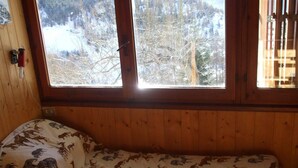 Habitación de cabaña de madera con una cama cubierta con un edredón estampado con animales, una ventana que da a un bosque nevado y un interruptor de luz fijado a la pared.