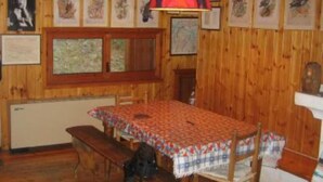 Interior de una cabaña de madera con una mesa de comedor, bancos y cuadros en las paredes.