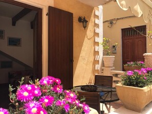 A sunlit patio with a wooden door, a metal table, and potted plants. - Villa in Lampedusa for two people,<br>proprietary<br>Nunzia (Lampedusa)
