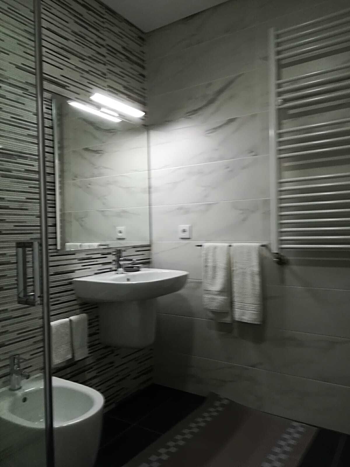 A modern bathroom with a glass shower enclosure, a pedestal sink, and a towel rack.