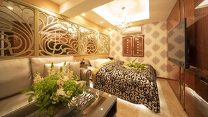 A hotel room with a sofa, a bed with a patterned bedspread, a decorative wall panel, a television, and a chandelier. - HOTEL G-Style - Adults Only (Tokyo)
