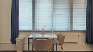 Ein Zimmer mit Tisch, zwei Stühlen, einem Heizkörper und einem Fenster mit Jalousien.