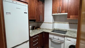 A compact kitchen with wooden cabinets, a white refrigerator, a stove, and a washing machine. - 2 Bedroom Apartament for rent next Atocha St. (Madrid)