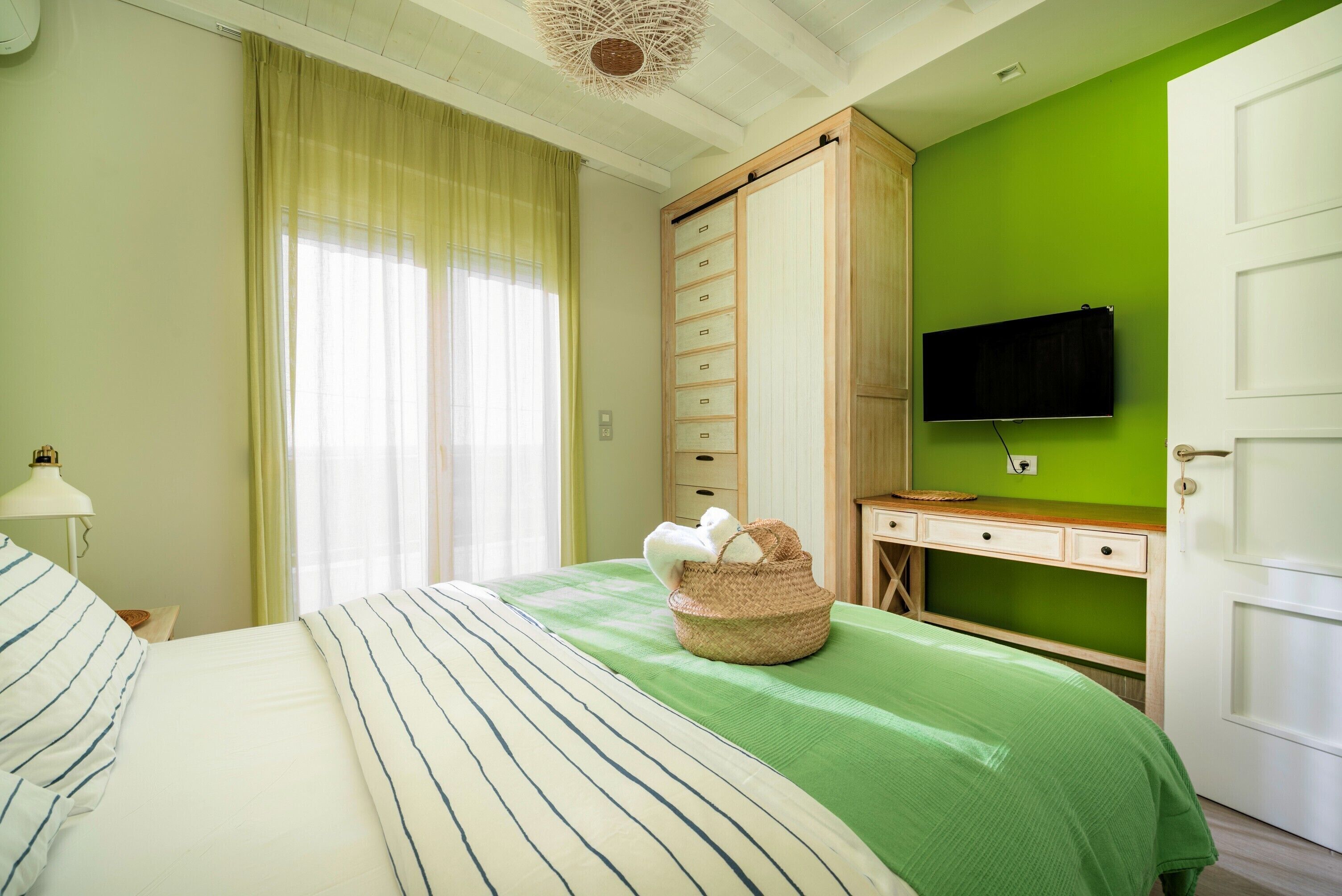 A bedroom with a bed, a green wall, a wooden wardrobe, a desk, and a television.
