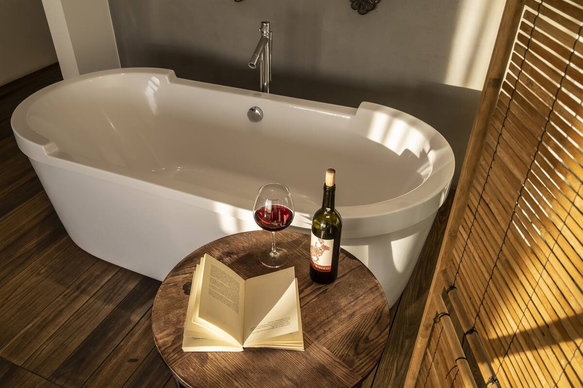 A bathtub with a wine bottle and glass on a wooden table.