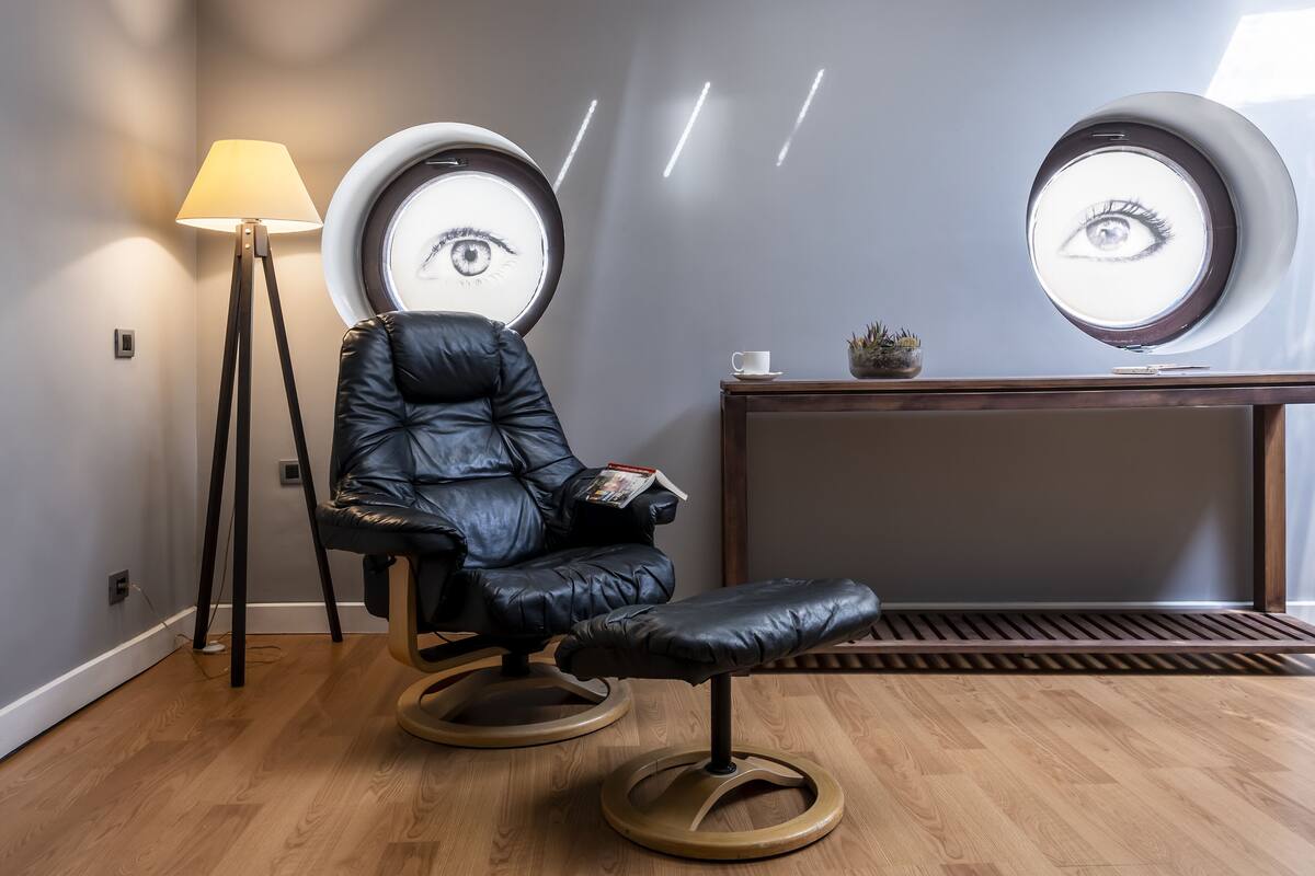 A modern room with a leather chair, a floor lamp, and a console table with a cup and a small plant.