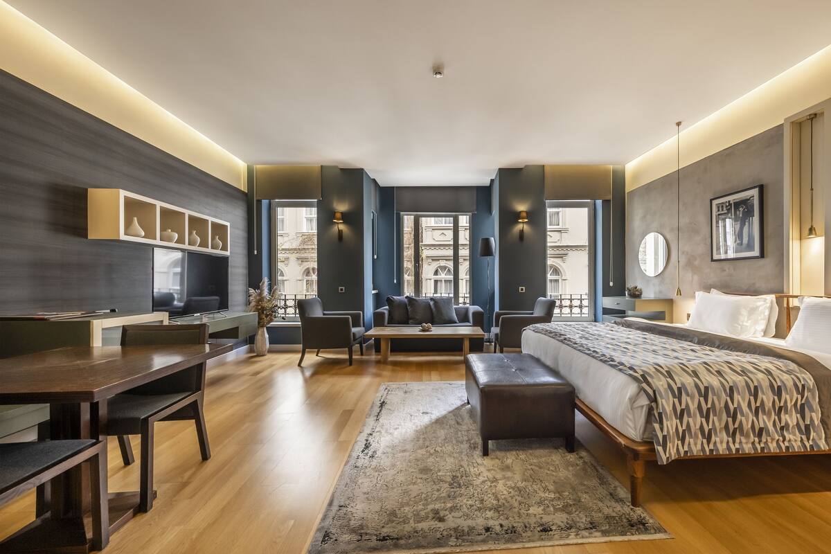 A modern hotel room with a large bed, a desk, a sofa, and a TV.