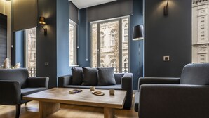 Una sala de estar moderna con un juego de sofá, una mesa de centro de madera y vistas a un edificio a través de grandes ventanales.