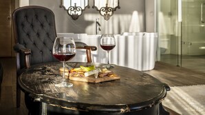 Una mesa de comedor con una copa de vino tinto y una tabla de quesos en una habitación moderna, con un sillón capitonado y espejos decorativos en la pared.