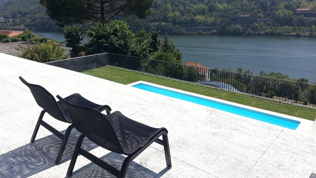 A poolside area with two lounge chairs and a view of a lake and hills.
