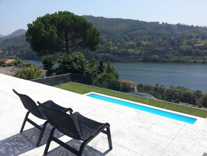 Un espace aménagé au bord de la piscine, avec deux chaises longues et une vue sur un lac et des collines.