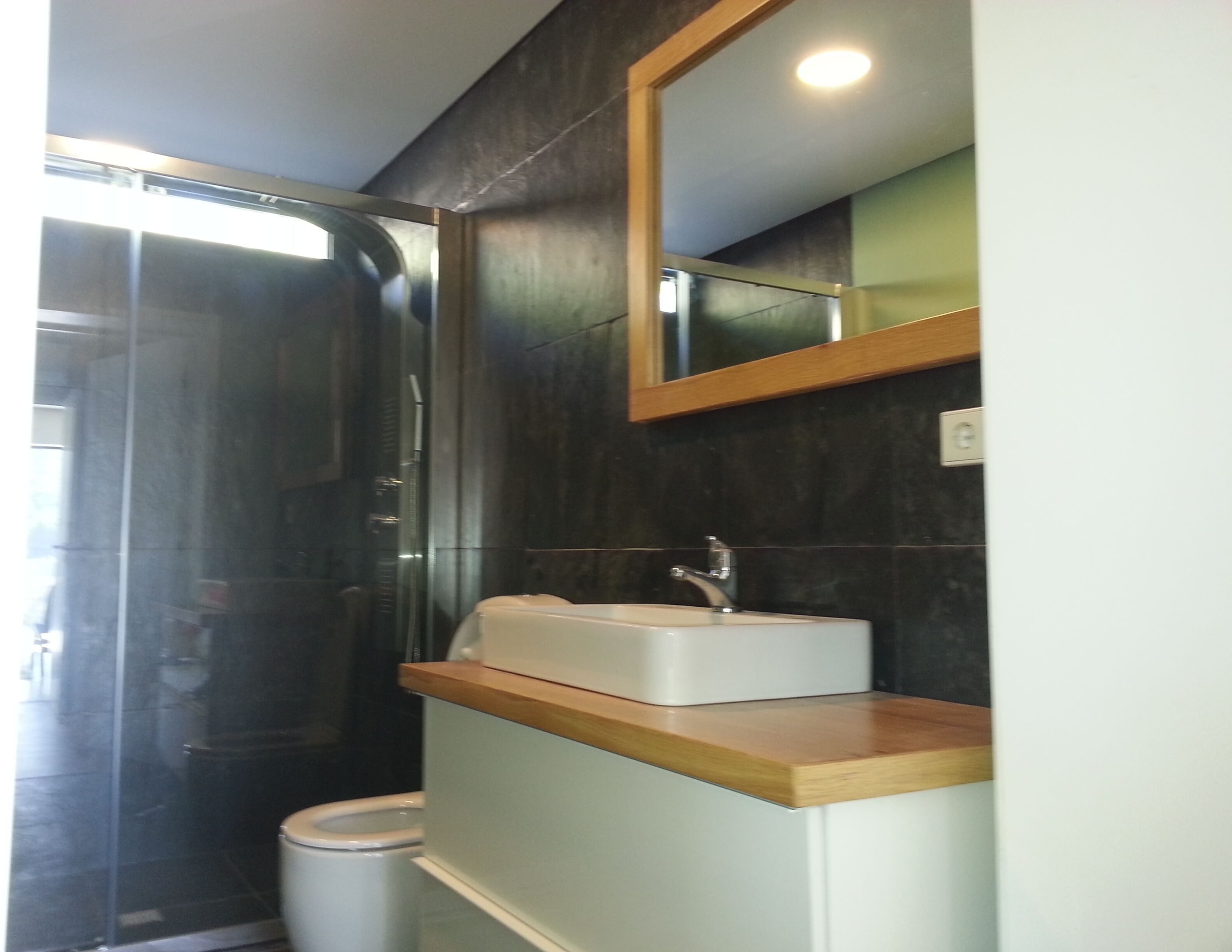 A bathroom with a glass shower enclosure, a white sink with a wooden countertop, and a mirror above the sink.