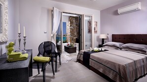 A modern hotel room with a bed, a desk with a chair, a small table with candles, and a view of a pool through an open door. - Villa Meadow 5 pax Private Infinity Pool  Beach Hotel Villa Paradise Naxos  (Naxos)