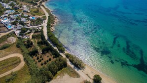An aerial view of a coastal area with a beach, clear blue waters, and a residential area with houses and a road. - Villa 'Blue' 10 pax Private Infinity Pool Beach Hotel Villa Paradise Naxos  (Naxos)