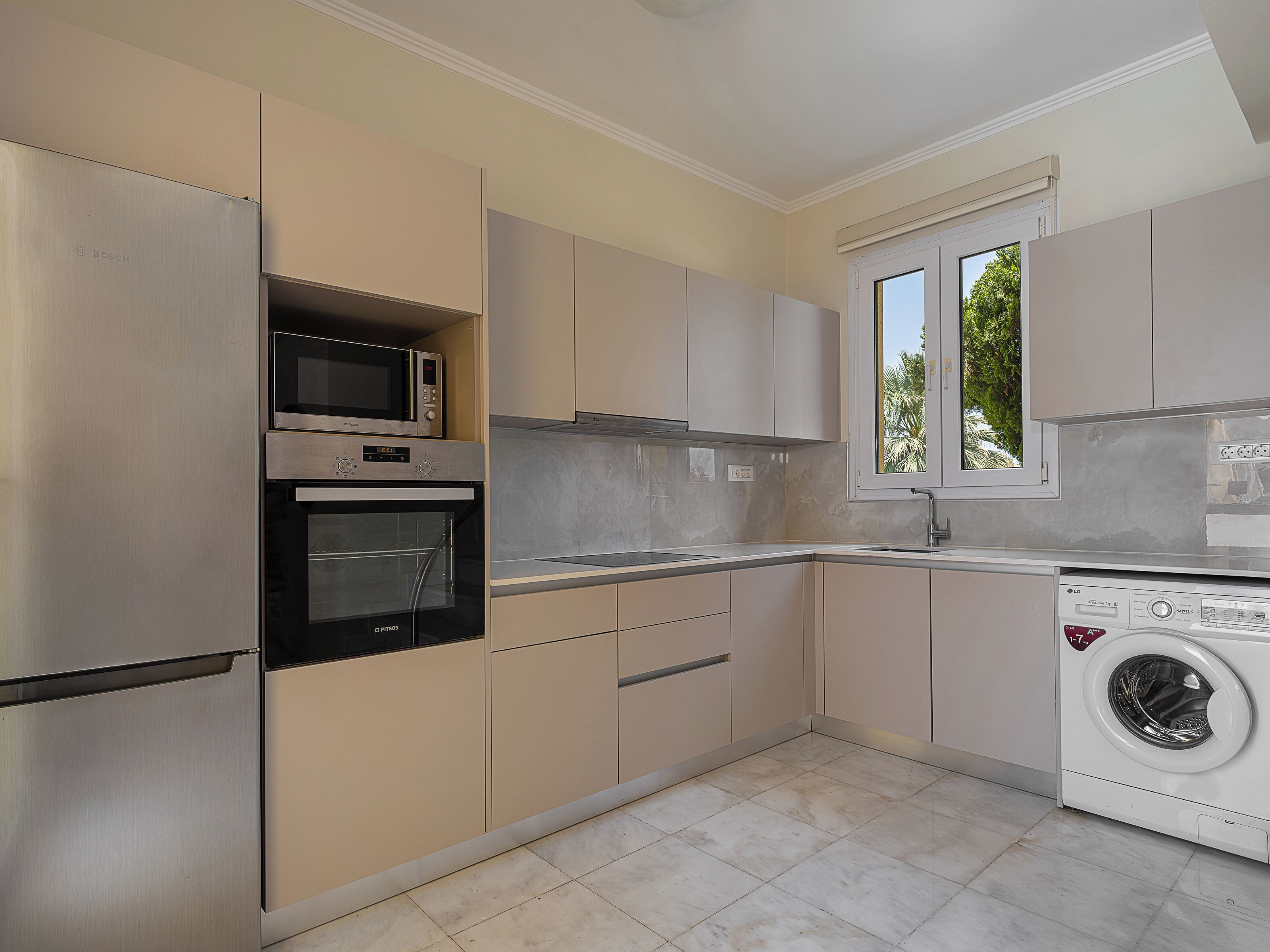A modern kitchen with stainless steel appliances, beige cabinetry, and a built-in washer and dryer.