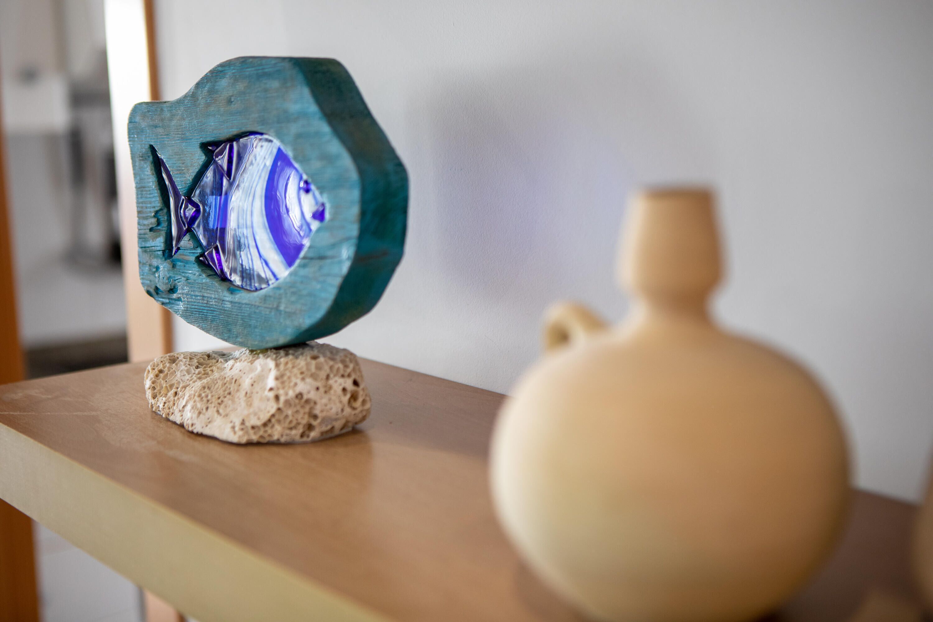 Een houten sculptuur met een vismotief op een gestructureerd oppervlak, een eenvoudige vaas en een houten tafel.