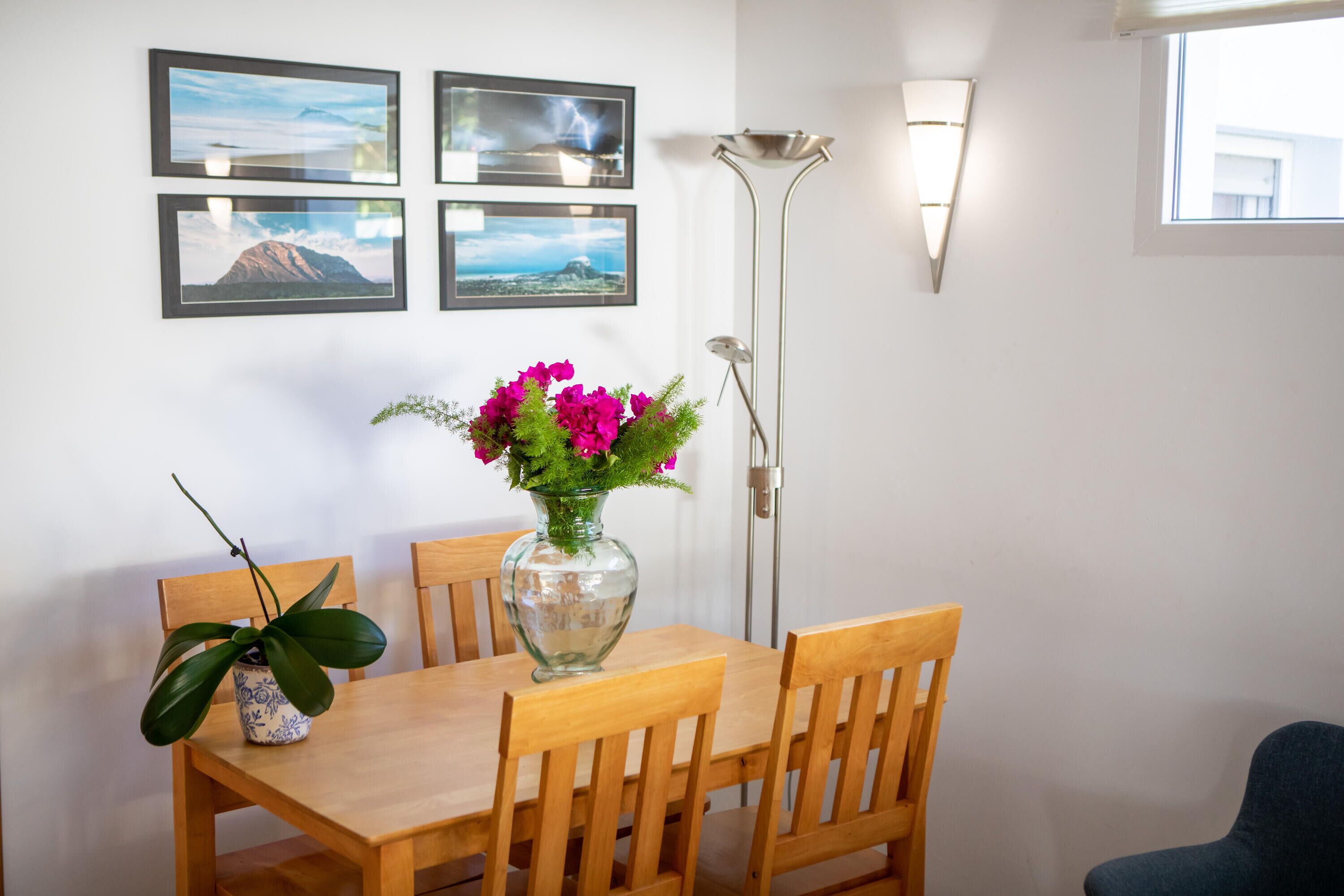 Uma sala de jantar com uma mesa e cadeiras de madeira, um vaso com flores e quadros nas paredes.