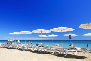 Een strand met witte ligbedden en parasols, een helderblauwe lucht en de oceaan op de achtergrond.
