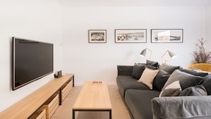A modern living room with a flat-screen TV, a wooden coffee table, a grey sofa with multiple cushions, and three framed pictures on the wall. - Nice duplex in the center of Terrassa (Barcelona) (Terrassa)