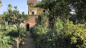 Un chemin de terre mène à un bâtiment doté d’un toit recouvert de tuiles rouges et de fenêtres en arc de cercle.