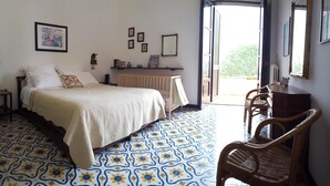 Une chambre à coucher comprenant un lit, une chaise, une commode et une porte donnant sur un balcon.