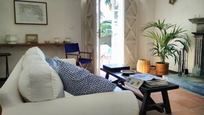 Un salon avec un canapé, un fauteuil, une table avec des livres, une plante en pot et une cheminée.