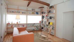 Un rincón acogedor para leer con una mecedora de madera, un banco acolchado y una estantería llena de libros.