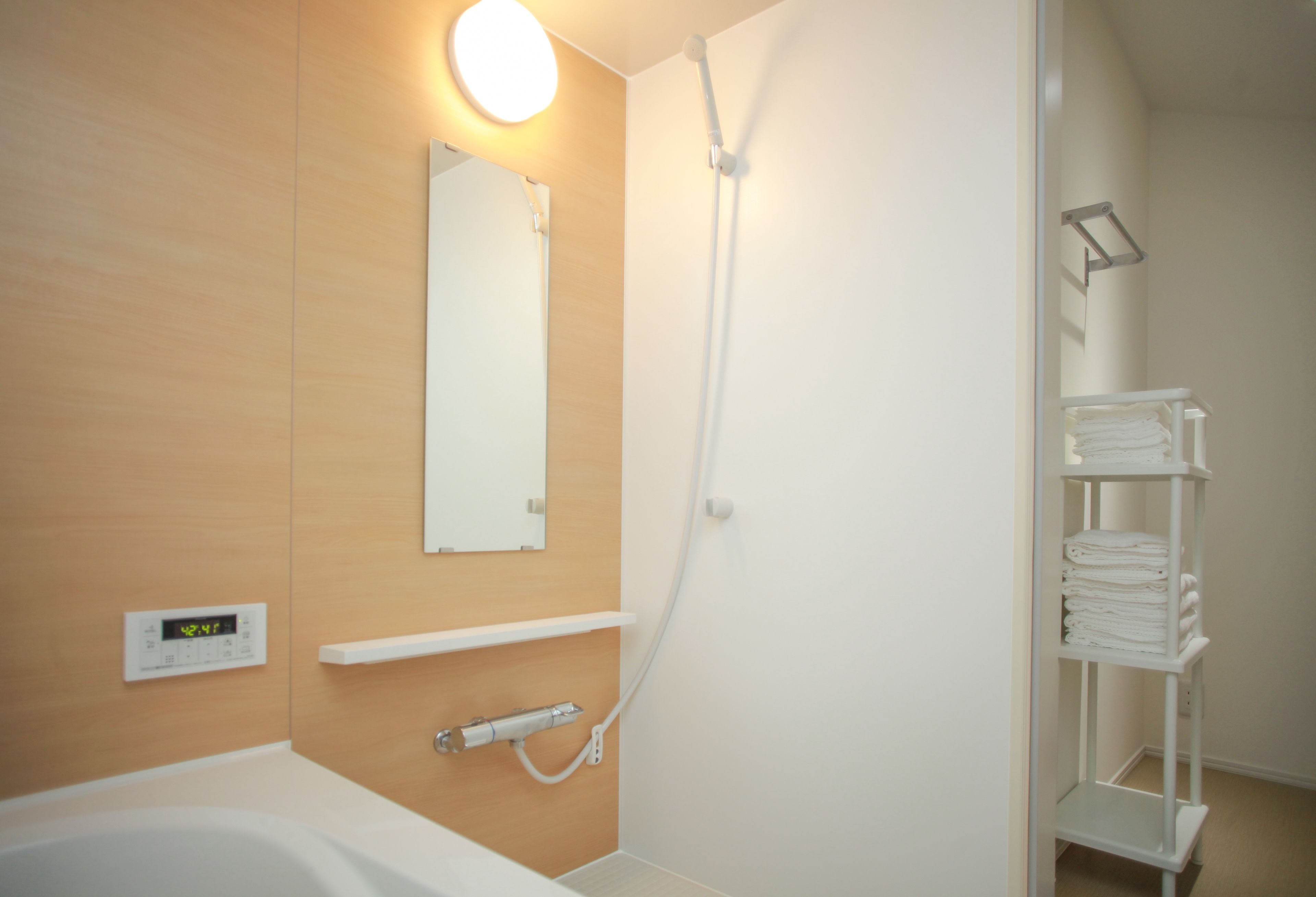 A modern bathroom with a bathtub, a shower, a wall-mounted thermostat, and a towel rack.