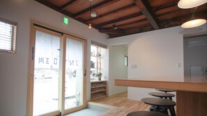 Una habitación con piso de madera, puerta de vidrio corredera que da al exterior, y un pequeño rincón con taburetes.