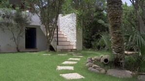 Un escalier en pierre menant à une porte, entouré d’une végétation luxuriante et d’un mur de pierre.