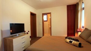 Ein Schlafzimmer mit einem Bett, einem Fernseher auf einer Kommode, einer Tür zu einem Badezimmer und einem Fenster mit Vorhängen.