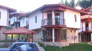 Ein Wohngebäude mit überdachter Terrasse, einer Stein-Fassade und einem Balkon mit Geländer.