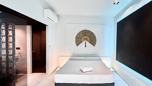 A modern bedroom with a bed, a wall-mounted air conditioner, a decorative fan, and a large window. - Blanca: Modern villa with private pool and garden (L'Escala)