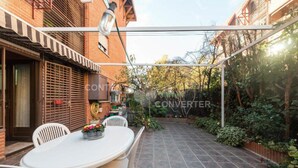 A covered patio with a table and chairs, surrounded by a brick wall and greenery.