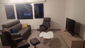 Ett vardagsrum med en soffa, två fåtöljer, ett soffbord, en tv och ett fönster med persienner.