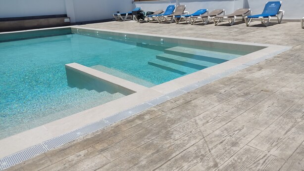 Ein Schwimmbecken mit klarem, blauem Wasser, umgeben von einer Holzterrasse und blauen Liegestühlen.