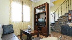 Ein Wohnzimmer mit einer Couch, einem Couchtisch, einem Fernseher auf einem Holzständer und einer Treppe mit einer Steinwand.