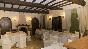 Zona de dinar amb diverses taules preparades per a menjar, amb teles de taula blanques i cadires, bigues de fusta al sostre i il·luminació penjada a la paret.