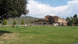 Zona exterior amb gespa, un tobogan i un edifici amb terrassa.