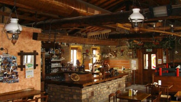 Un bar rústic amb bigues de fusta, parets de pedra i llums penjants.