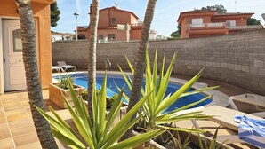 Area piscina con sedie a sdraio, una palma e un edificio sullo sfondo.