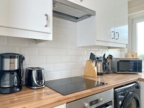 Une cuisine moderne avec des meubles blancs, une plaque de cuisson à induction noire, une machine à café, un grille-pain, un four à micro-ondes et un lave-vaisselle.
