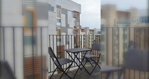 Un balcón con mesa y sillas, un edificio moderno con fachada decorativa y vistas a edificios cercanos.