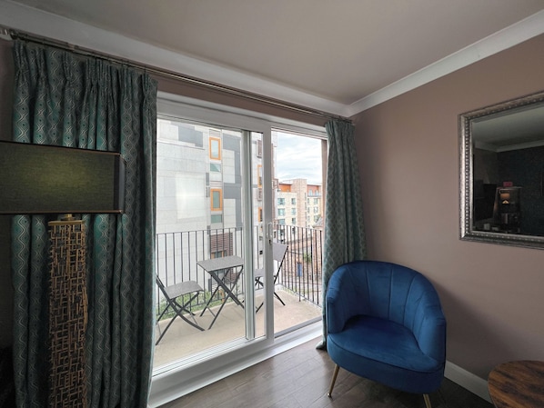 A room with a sliding glass door leading to a balcony, a blue armchair, and a mirror on the wall. - Boutique Apartment on Royal Mile - Sleeps 3 (Edinburgh)