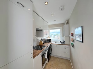 Cocina compacta con armarios blancos, microondas, estufa y ventana con vistas a edificios.