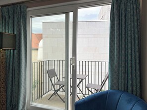 Un balcon avec deux chaises et un canapé bleu, une porte-fenêtre coulissante et des rideaux à motifs.
