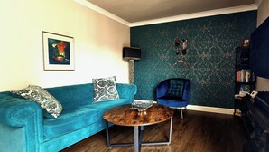 A room with a teal sofa, a small wooden coffee table, a blue armchair, a bookshelf, and a TV mounted on the wall. - Boutique Apartment on Royal Mile - Sleeps 3 (Edinburgh)