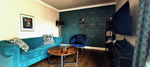 A room with a teal sofa, a small wooden coffee table, a blue armchair, a bookshelf, and a TV mounted on the wall. - Boutique Apartment on Royal Mile - Sleeps 3 (Edinburgh)